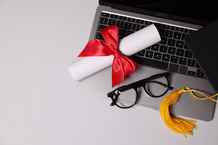 Graduation cap, diploma, laptop and glasses on light table, top viewの写真素材