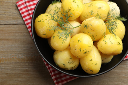 Tasty young boiled potatoes with dill and oil in bowl on wooden table, top viewの写真素材