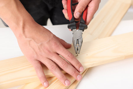 Man pulling metal nail out of wooden plank with pincers indoors, closeupの写真素材