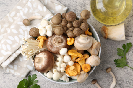 Different raw mushrooms in bowl, parsley and oil on gray textured table, flat layの写真素材