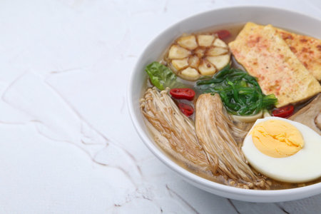 Tasty ramen with enoki and king oyster (eryngii) mushrooms on white table, closeup. Space for textの写真素材