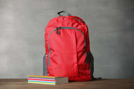 Red backpack and notebooks on wooden table against gray background. Space for textの写真素材