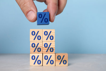 Man putting blue cube with percent sign onto others against light blue background, closeupの写真素材