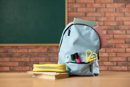 Light blue backpack with different stationery, pencil case and book on desk in classroomの写真素材