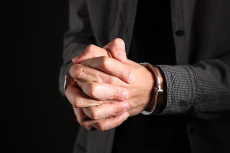 Man in metal handcuffs on black background, closeupの写真素材