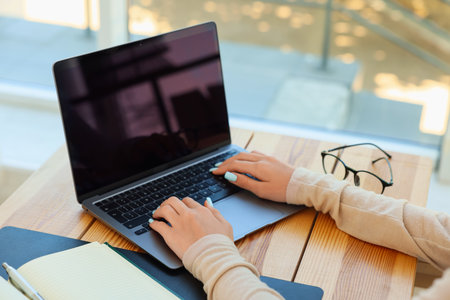 Teenage girl using laptop at wooden desk indoors, closeup. Home workplaceの写真素材