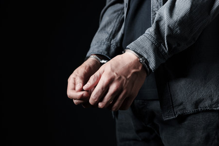 Man in metal handcuffs on black background, closeup. Space for textの写真素材