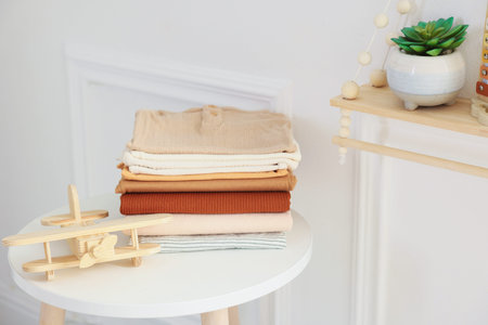 Stack of clean baby clothes and toys on white table indoors, space for textの写真素材