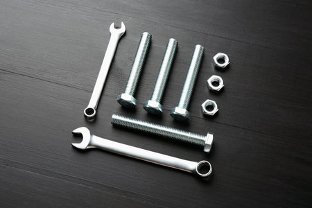 Many metal wrenches, bolts and nuts on black wooden table, flat lay