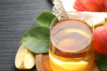 Fresh cider in glass, apples and green leaves on black textured table, closeupの写真素材