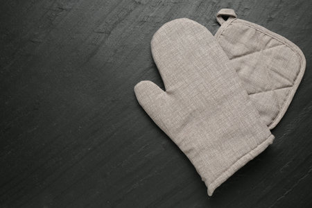 Grey oven glove and potholder on dark textured table, top view. Space for textの写真素材