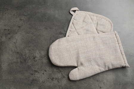 Grey oven glove and potholder on dark textured table, top view. Space for textの写真素材