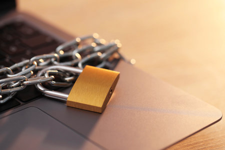 Cyber safety. Metal padlock with chain and laptop on table, closeupの写真素材