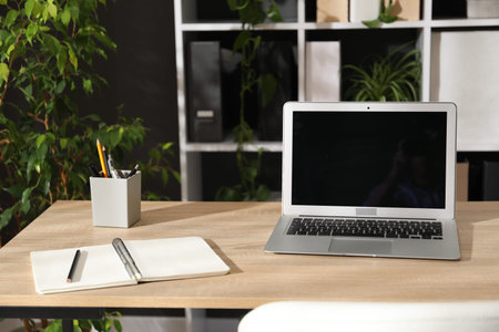 Stylish workplace with laptop, stationery and floral decor in office. Biophilic interior design