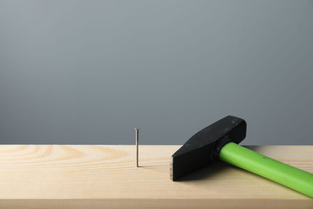 Metal nail in wooden plank and hammer on gray background, closeupの写真素材
