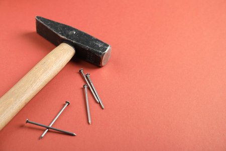 Metal nails and hammer on coral background, closeup. Space for text