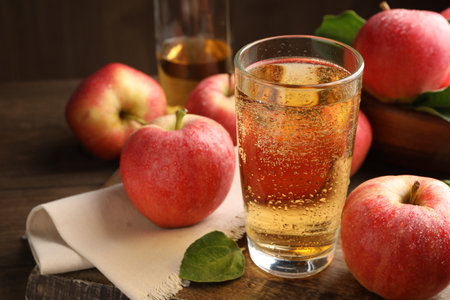 Delicious cider in glass, apples and leaves on wooden table, closeupの写真素材