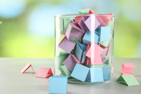 Colorful paper pieces in glass jar on wooden table against blurred background, closeup