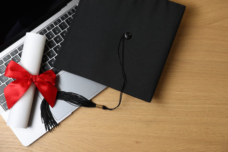 Graduation cap, laptop and diploma on wooden table, flat lay. Space for textの写真素材
