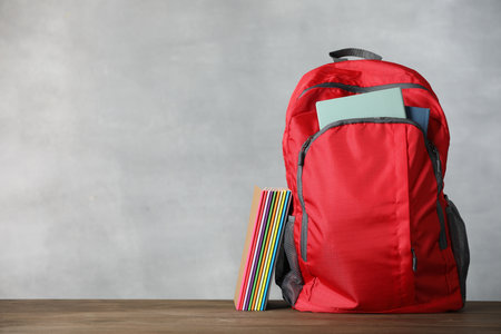 Red backpack and notebooks on wooden table against gray background. Space for textの写真素材