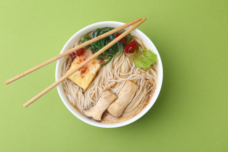 Tasty ramen with enoki and king oyster (eryngii) mushrooms on green background, top view
