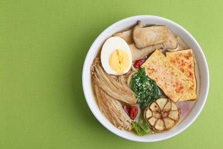 Tasty ramen with enoki and king oyster (eryngii) mushrooms on green background, top view. Space for...