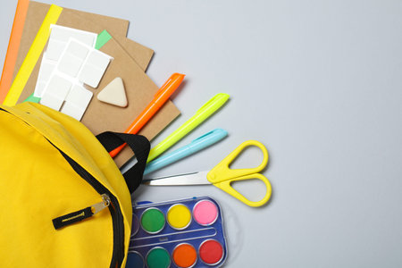 Yellow school backpack with different stationery on gray background, flat lay. Space for text