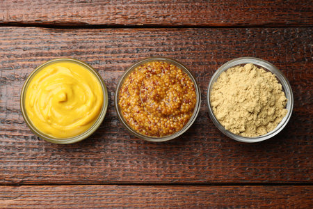 Different types of mustard on wooden table, flat layの写真素材
