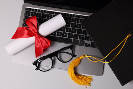 Graduation cap, diploma, laptop and glasses on light table, flat layの写真素材