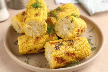Pieces of tasty grilled corncobs with dill on wooden table, closeup