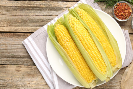 Tasty boiled corncobs and spices on wooden table, flat lay. Space for text