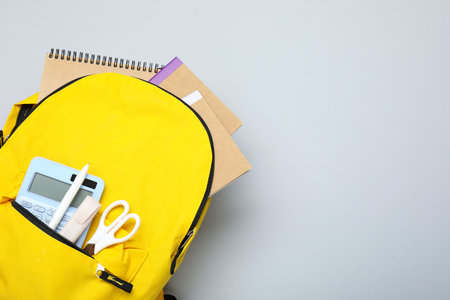 Yellow school backpack with different stationery on gray background, above view. Space for textの写真素材