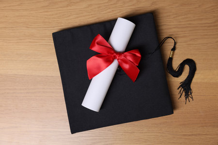 Graduation cap and diploma on wooden table, top viewの写真素材