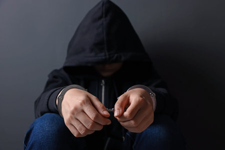 Woman in metal handcuffs and hoodie near gray wall