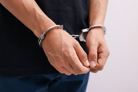 Man in metal handcuffs on light background, closeupの写真素材