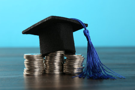 Scholarship. Graduate hat and coins on wooden table against light blue background, closeupの写真素材