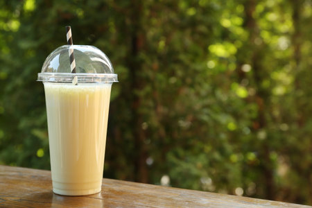 Tasty milkshake in plastic cup on wooden table outdoors, space for textの写真素材