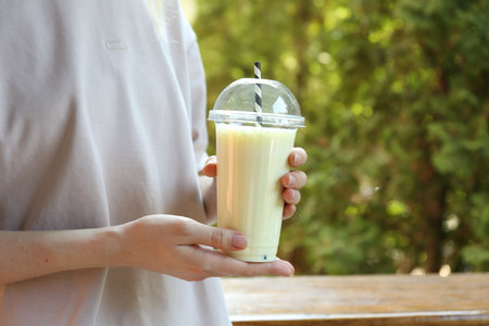 Woman holding tasty milkshake in plastic cup outdoors, closeupの写真素材