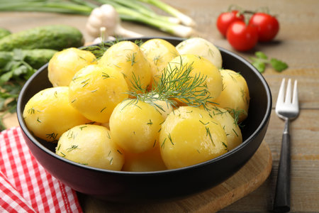 Tasty young boiled potatoes with dill and oil in bowl on wooden table, closeupの写真素材