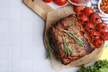Delicious roast beef with rosemary, tomatoes and other products on white tiled table, flat lay. Space for textの写真素材