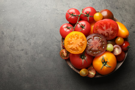Different ripe tomatoes in bowl on gray table, top view. Space for textの写真素材