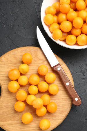 Ripe yellow cherry plums, wooden board and knife on black table, flat layの写真素材