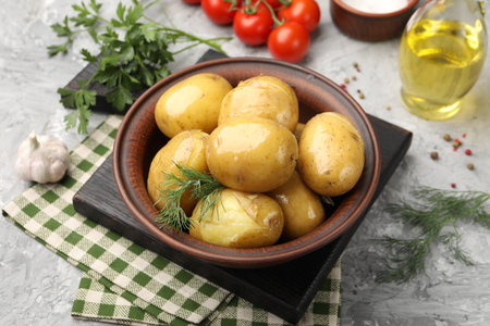 Tasty young boiled potatoes with dill, oil in bowl and products on gray textured table, closeupの写真素材