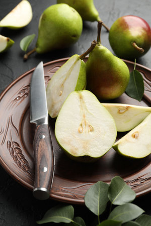 Fresh ripe pears, knife and green leaves on black table, closeupの写真素材