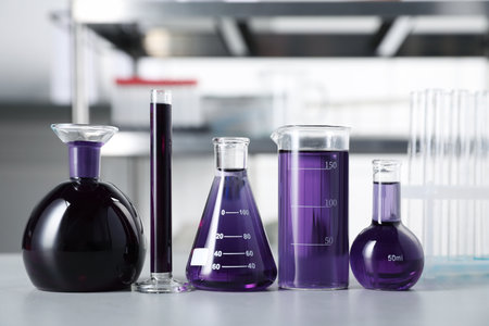 Different laboratory glassware with purple liquid on light table indoorsの写真素材