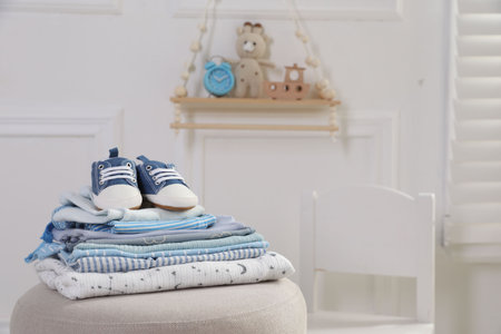 Stack of clean baby clothes and shoes on pouf indoors, space for textの写真素材