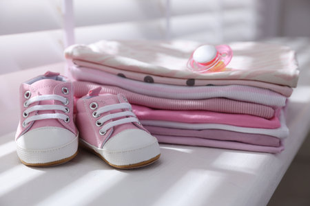 Stack of clean baby clothes, shoes and accessory on window sill indoors, closeupの写真素材