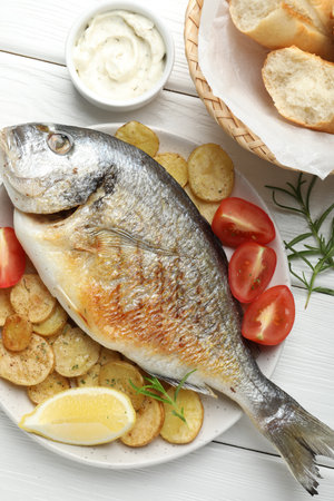 Tasty roasted dorado fish served with vegetables and sauce on white wooden table, flat lay. Homemade seafood dishの写真素材
