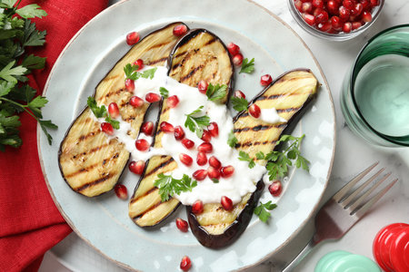 Slices of grilled eggplant with pomegranate seeds and yoghurt on white marble table, flat layの写真素材