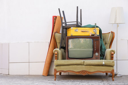 Retro TV on sofa and other used stuff near white wall outdoorsの写真素材